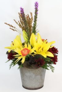 A rustic fall garden look in a metal tin featuring Asiatic lilies, spider mums, orange carnations, fall daisies and fall accents.
