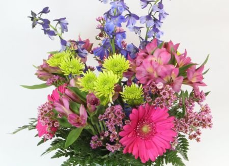 A spring bouquet filled with gerbera daisies, delphinium, Peruvian lilies, kermits and more in a dimpled glass vase.