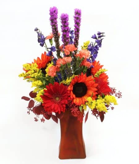 Bold flower arrangement with red sunflowers and gerbera daisies and other seasonal blooms in varying colors.