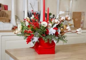 Christmas or New Year home decor with red candle, fir branches, berries and flowers. Winter holiday celebration, festive table center in a box close up
